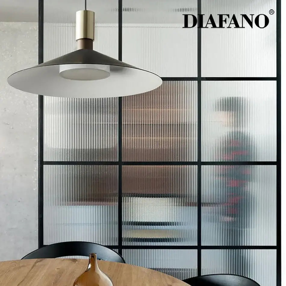 Minimalist gray and brass decorbites dimming pendant light with matte black conical shade above wooden table