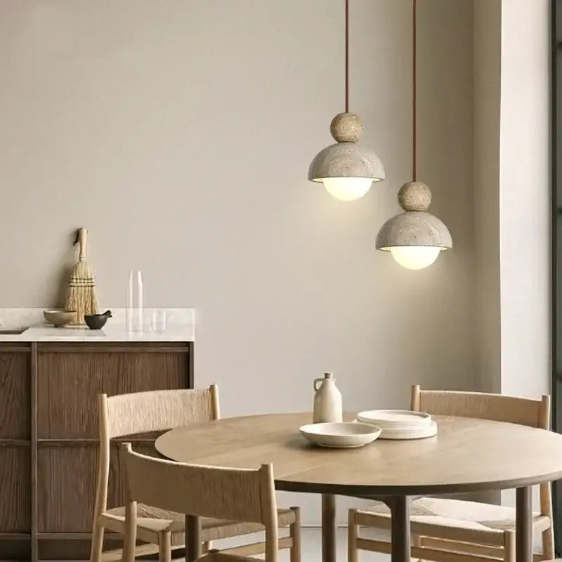 Two minimalist gray concrete glass ball pendant lights with warm bulbs hang above a wooden dining table decorbites glass ball pendant light