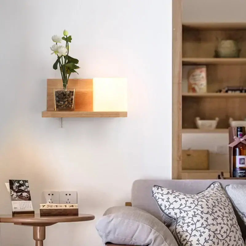 Minimalist led wooden wall lamp with pull chain switch illuminating a wooden shelf with a glass vase and white flowers