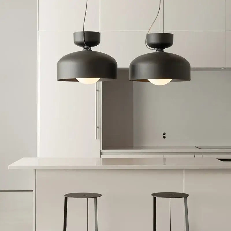 Two matte black minimalist pendant lights with decorbites forged iron hang above a white kitchen island