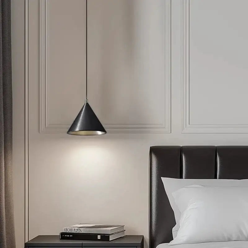 Minimalist matte black pendant light chandelier with metallic interior hanging above a dark leather headboard