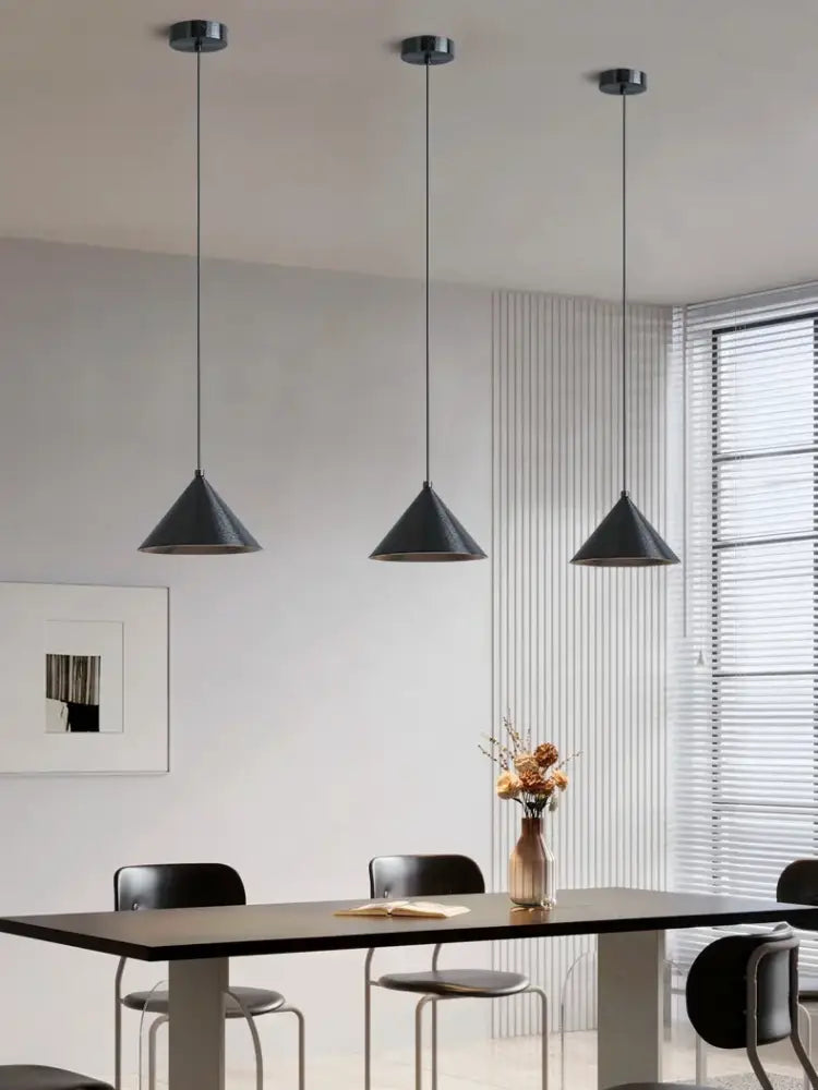Three sleek black conical pendant lights with metallic fixtures form a minimalist matte black pendant light chandelier for dining room