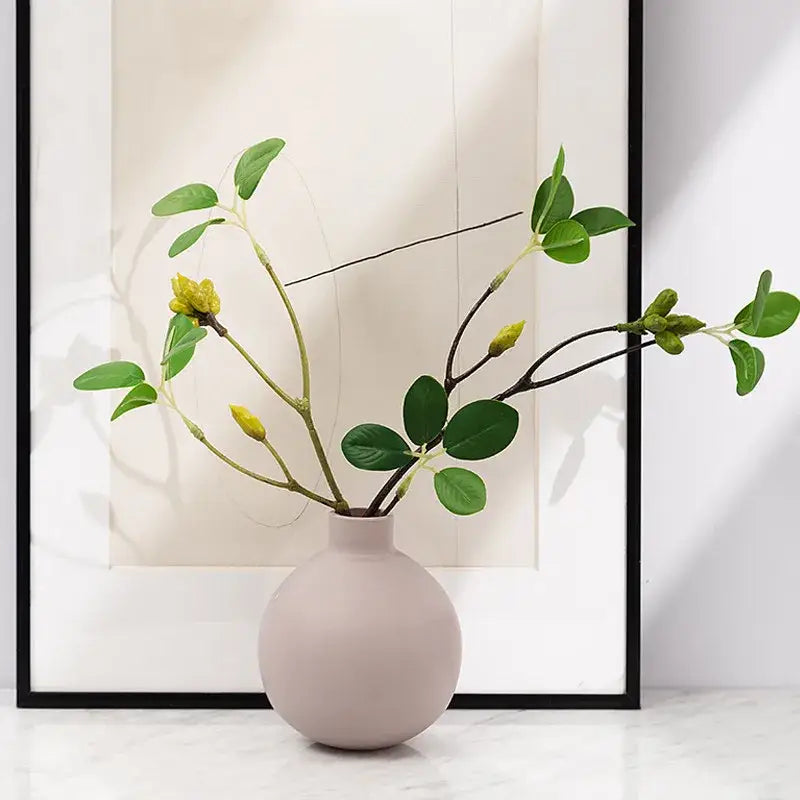 A minimalist matte blush pink geometric ceramic vase by decorbites holding artificial green branches with yellow buds