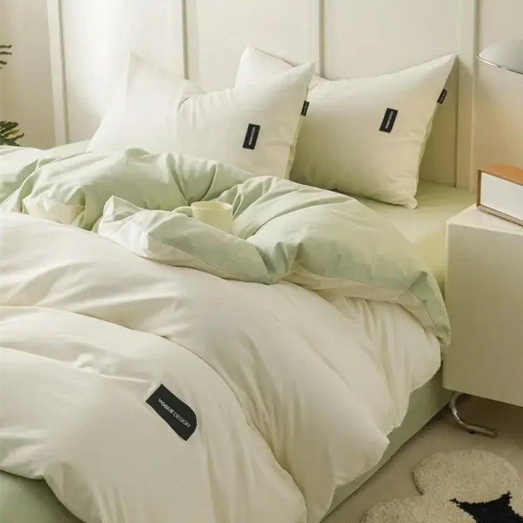 Minimalist off-white and soft mint green matching cotton bedding set with subtle black brand tags on duvet and pillows