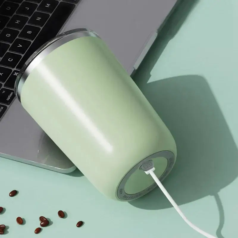 A sleek matte mint-green minimalist pastel electric magnetic stirring coffee cup with a white charging cable plugged in