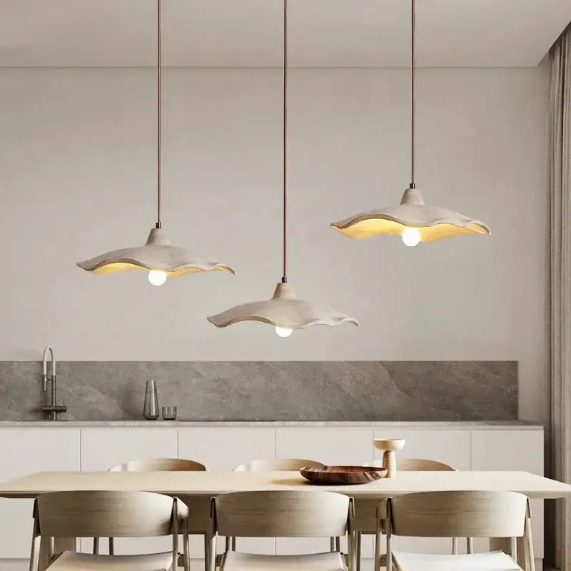 Three off-white ceramic pendant chandeliers with scalloped edges hang above a dining table in minimalist decorbites concrete high style