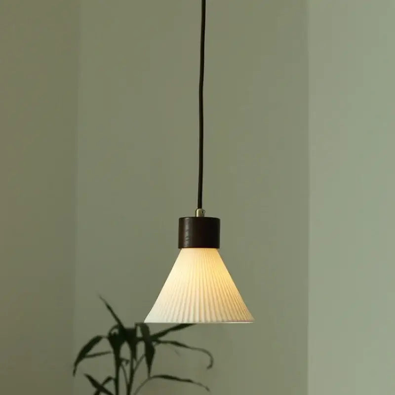 Minimalist pleated glass and wood pendant light fixture with off-white shade and dark wood top for kitchen use