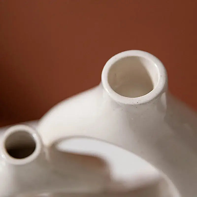 White ceramic teapot with smooth glossy finish and two spouts paired with minimalist speckled off-white ceramic donut candle holder decorbites ceramic donut candle decor