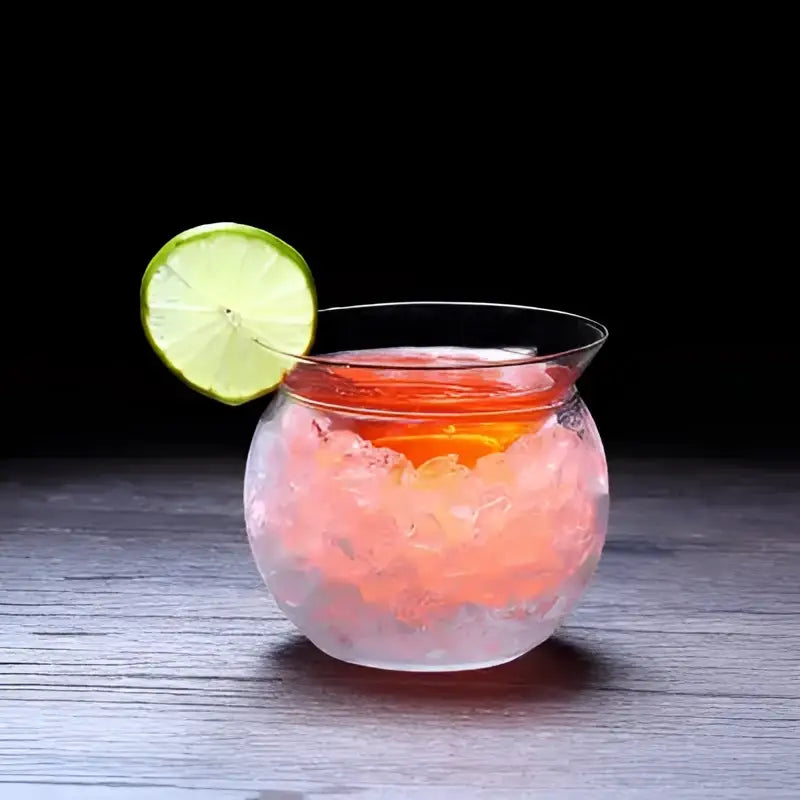 A clear glass 150ml stemless martini chiller filled with pinkish-orange liquid and ice garnished with a lime slice