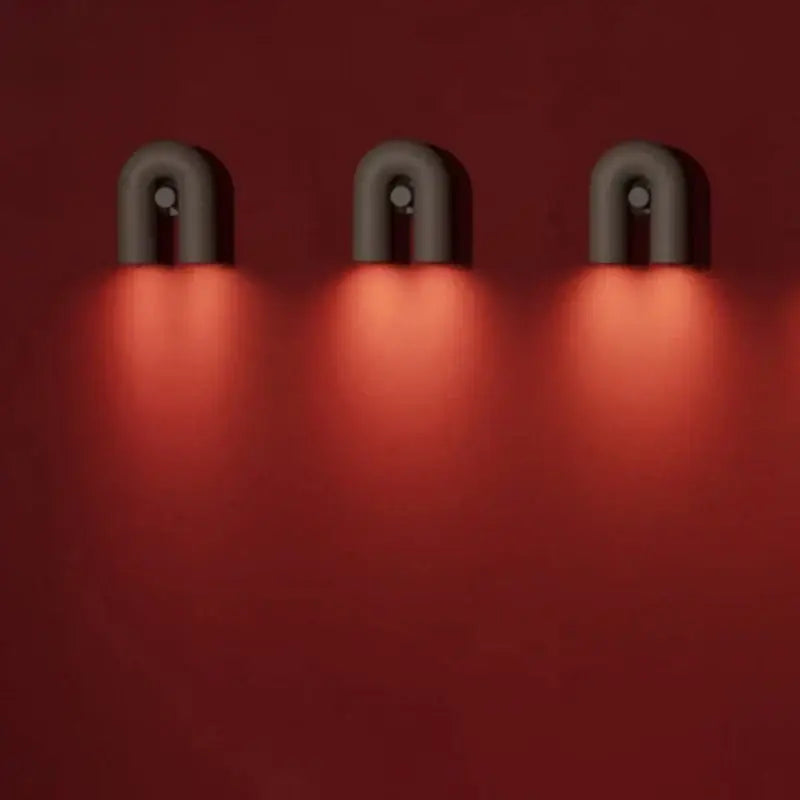 Three sleek matte black minimalist terracotta cirkus tube wall sconces emit a warm red glow for bedroom reading light