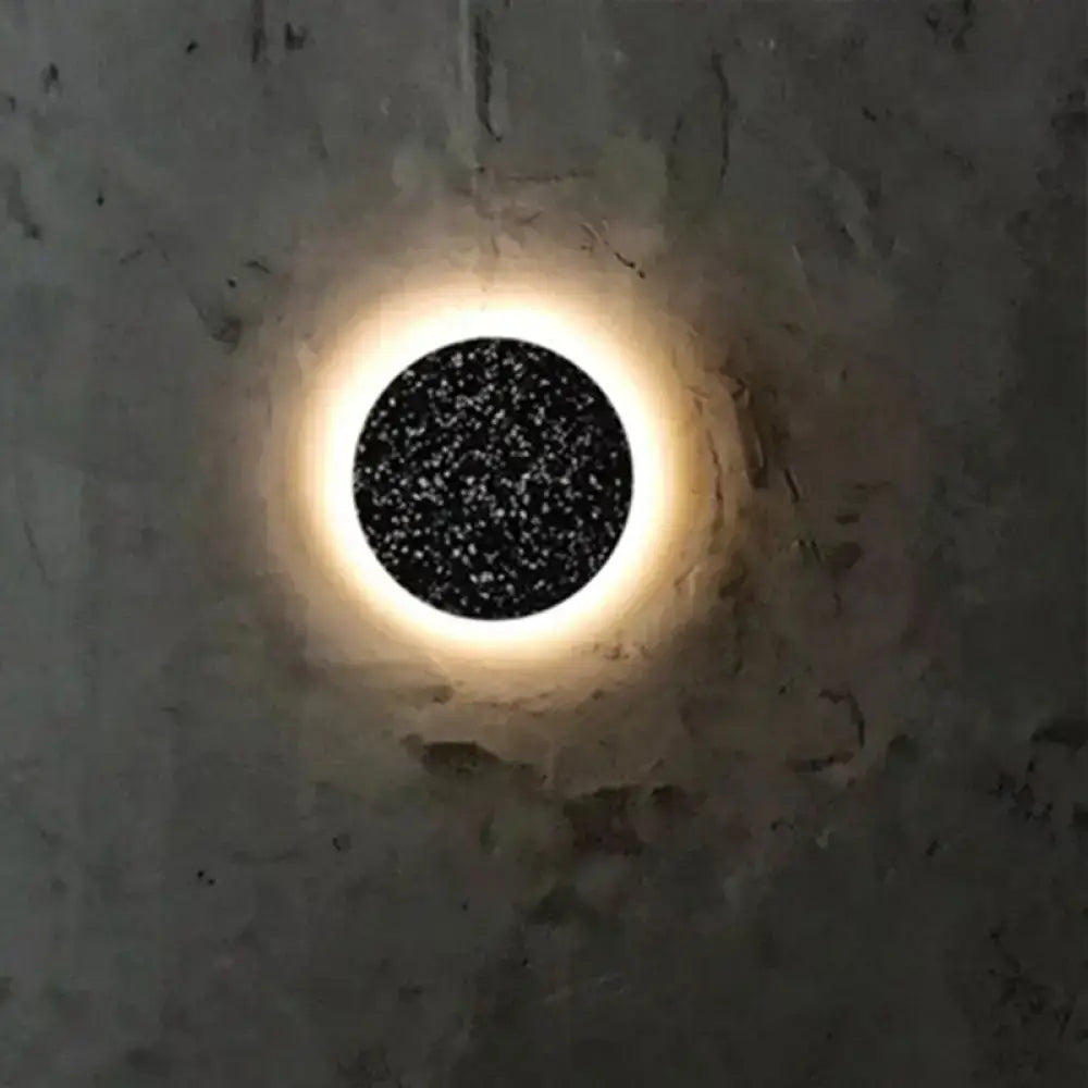 Minimalist terrazzo round LED wall sconce with glowing black star-speckled center and illuminated halo on concrete wall