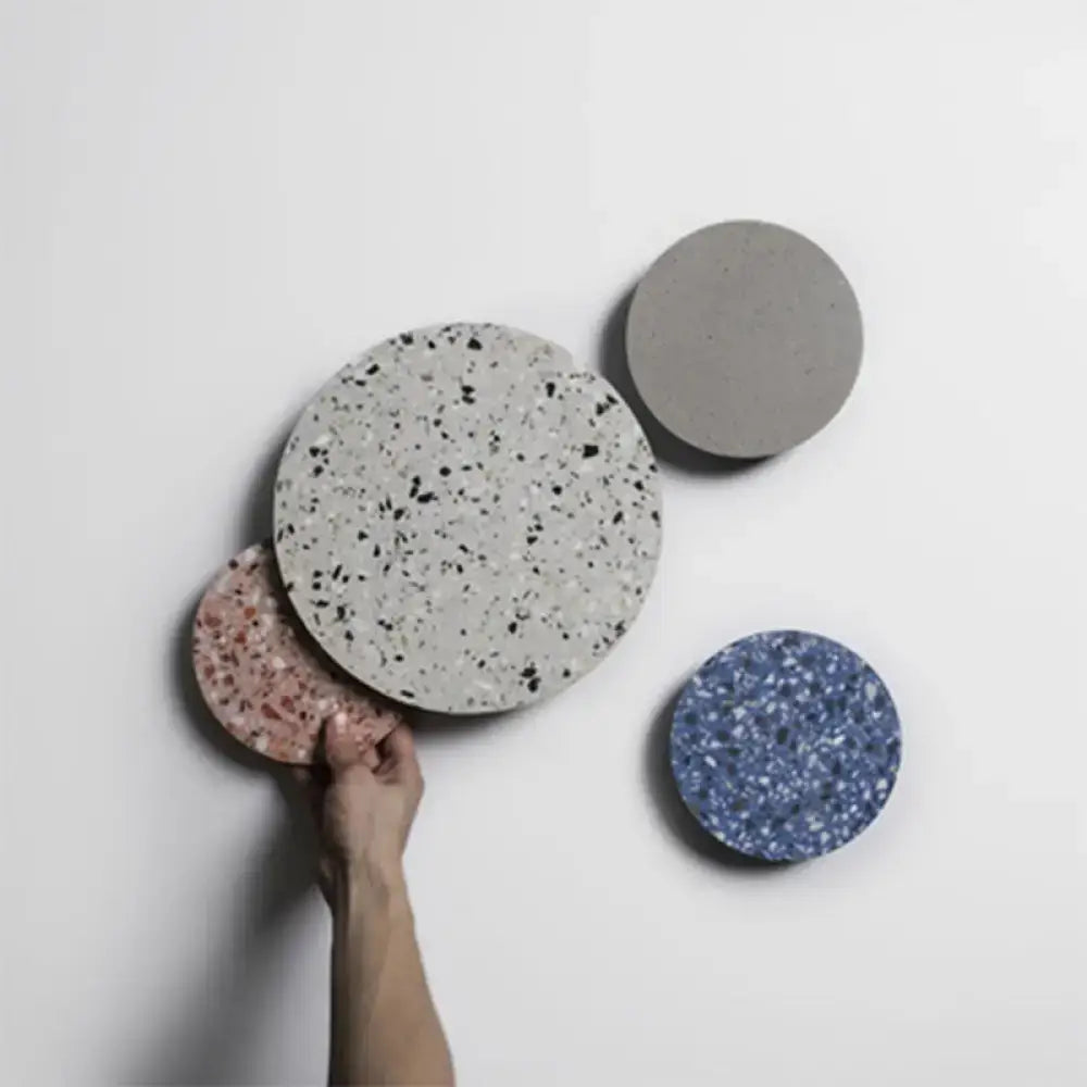 A hand holds a minimalist terrazzo round led wall sconce with a speckled gray and black terrazzo surface for bedroom lighting
