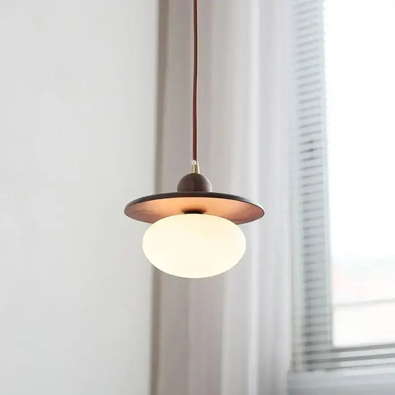 Minimalist walnut and brass glass led pendant lamp with warm brass shade and white globe bulb suspended by dark cord