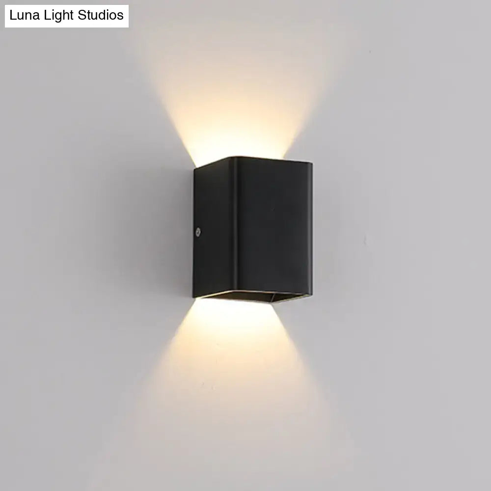 Black rectangular wall lamp with cube shade and brass accents emitting warm light for modern bedroom use