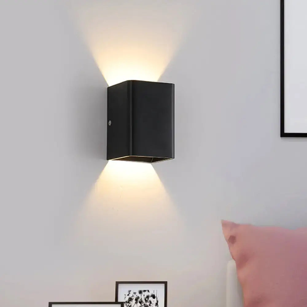 Black rectangular wall lamp with cube shade and brass accents projecting two angled white light beams