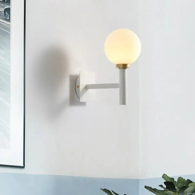 Minimalist white and brass wall lamp with opal glass shade featuring a frosted globe for bedroom lighting