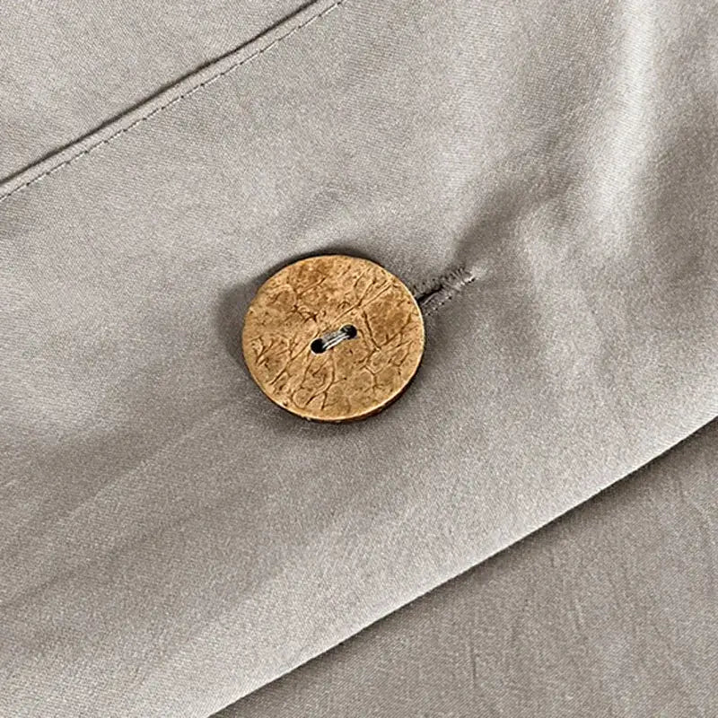 A round light brown cork button with two dark metal holes on a minimalist white buttoned washed cotton bedding set