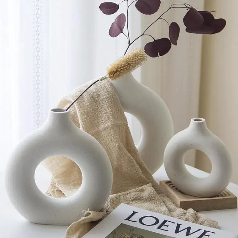 Minimalist white decorbites ceramic donut vase set with circular cutouts holding dried eucalyptus and a brush