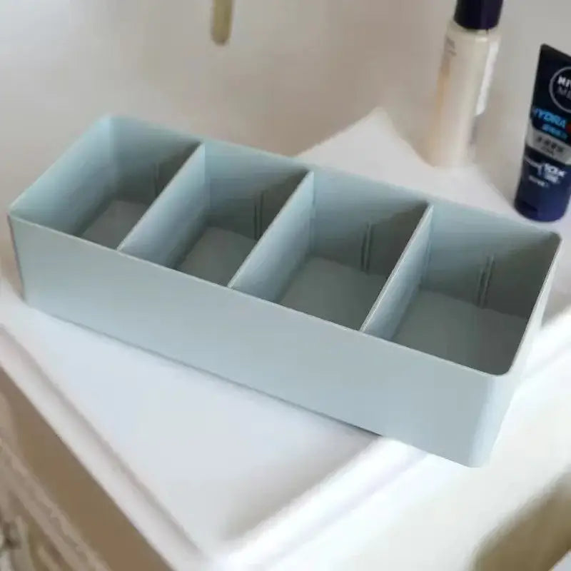 Light blue smooth plastic divided storage box with four compartments for minimalist kitchen tableware organization