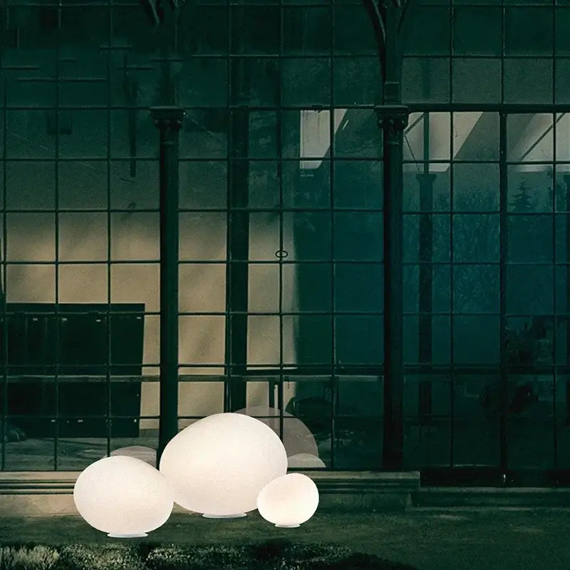 Minimalist white egg glass floor lamp with three glowing spherical lamps for living room near dark glass window