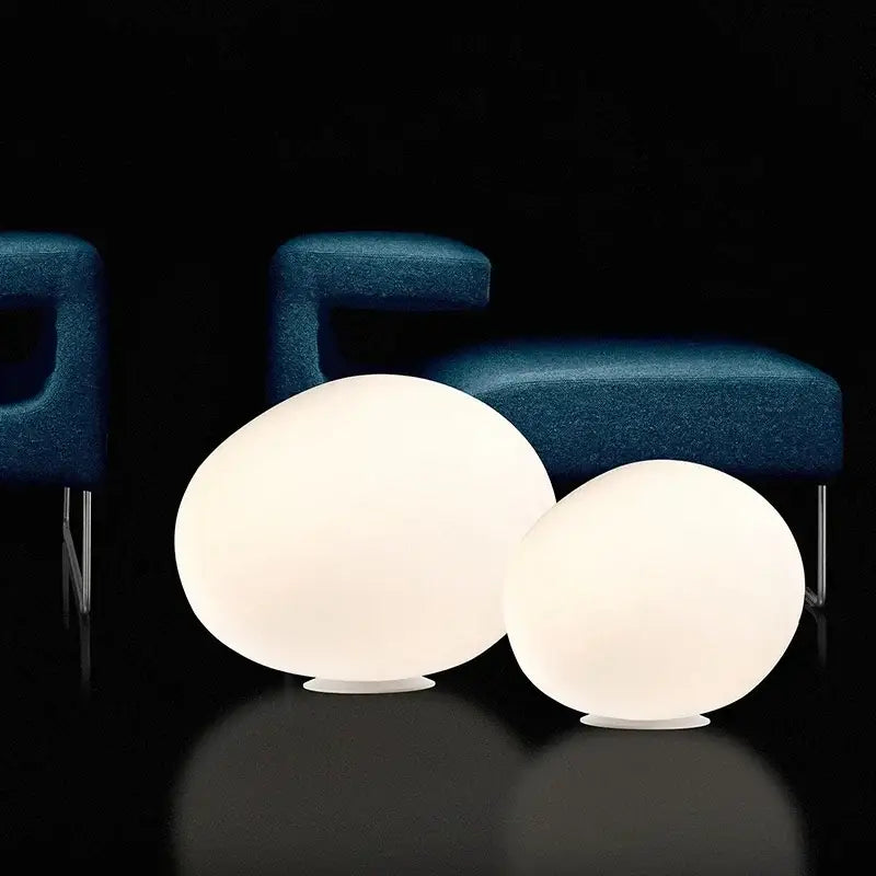 Two glowing minimalist white egg glass floor lamps with frosted glass surfaces and metallic bases for living room use