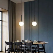 Two minimalist white glass ball pendant lights with black fixtures hang above a dining table decorbites glass ball