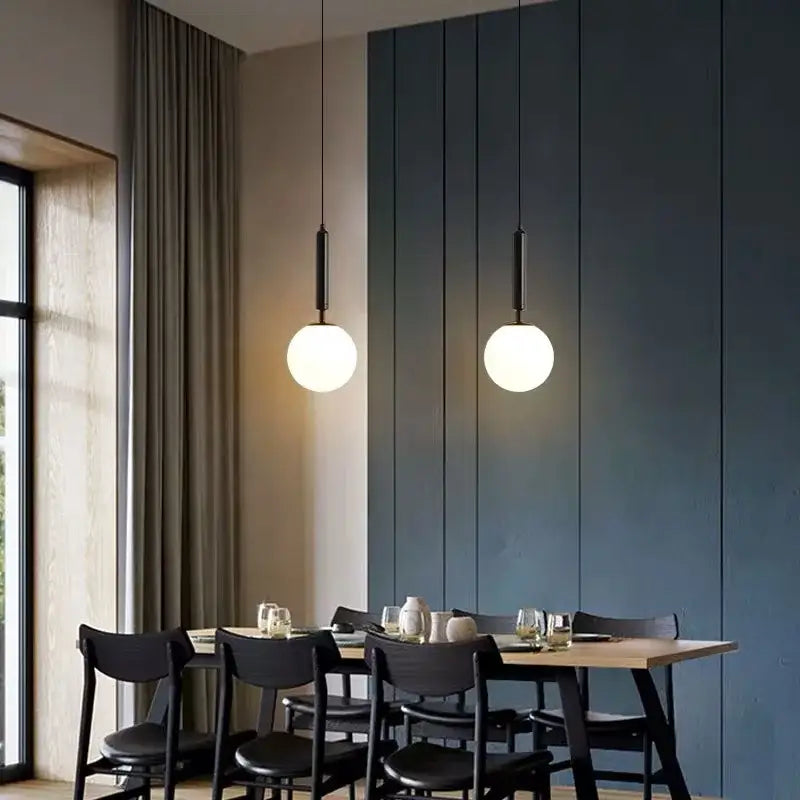 Two minimalist white glass ball pendant lights with black fixtures hang above a dining table decorbites glass ball