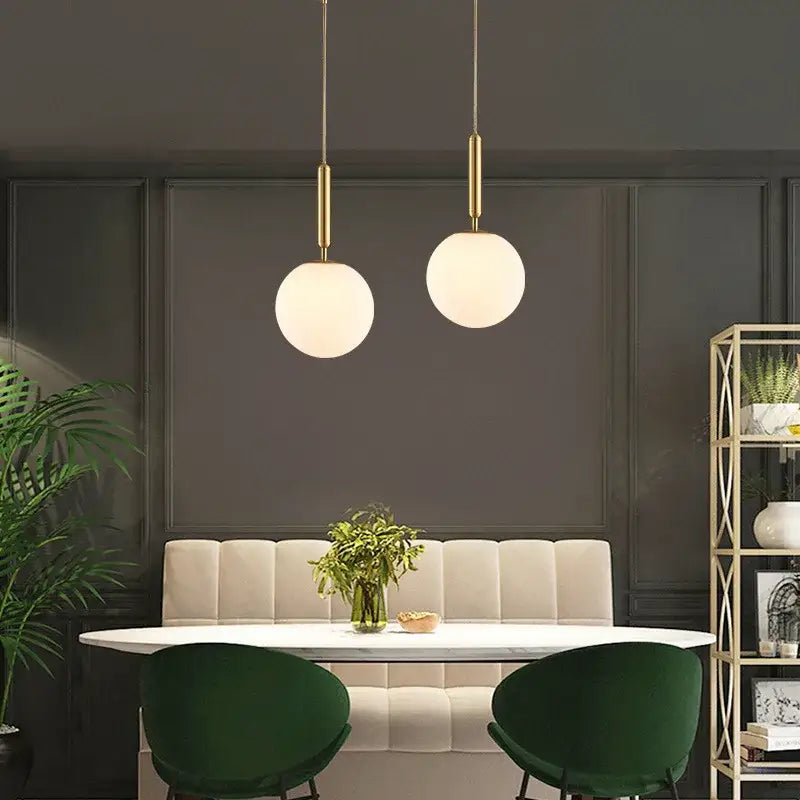 Two minimalist white glass ball pendant lights with gold-toned fixtures hang above a dining room table decorbites glass ball pendant