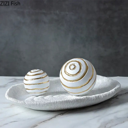 Minimalist white ceramic spheres with gold spiral stripes on textured tray for geometric desk decoration and living room art