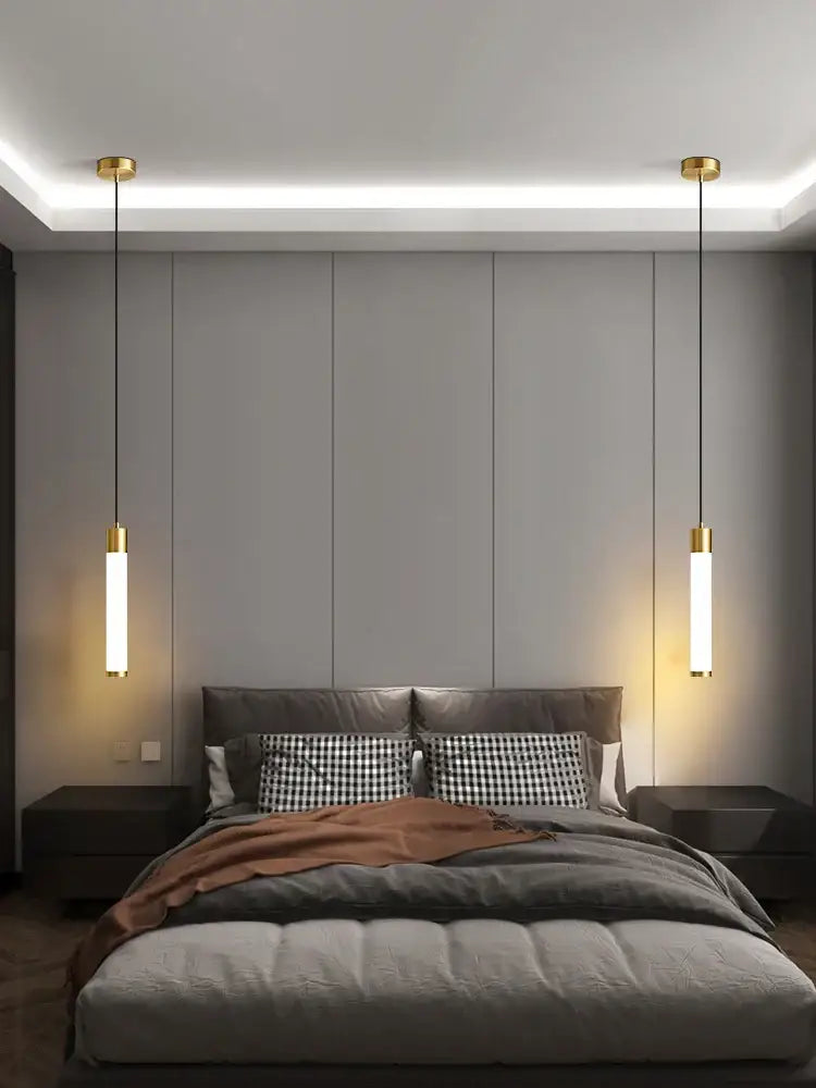 Gold-finished linear pendant light with frosted glass shades and white finish hanging symmetrically above the bed