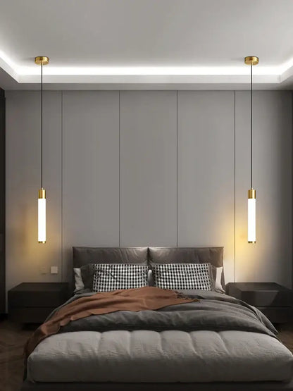 Gold-finished linear pendant light with frosted glass shades and white finish hanging symmetrically above the bed