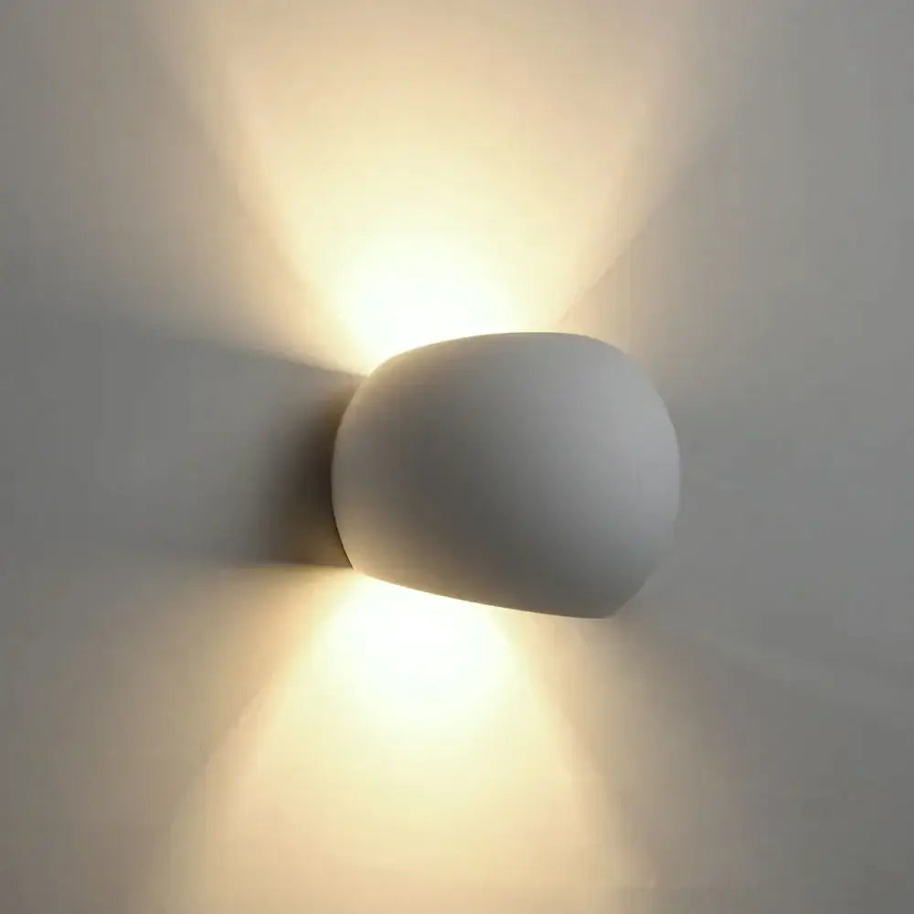 A sleek matte white gypsum wall lamp with rounded design emitting warm diffused light for living room use