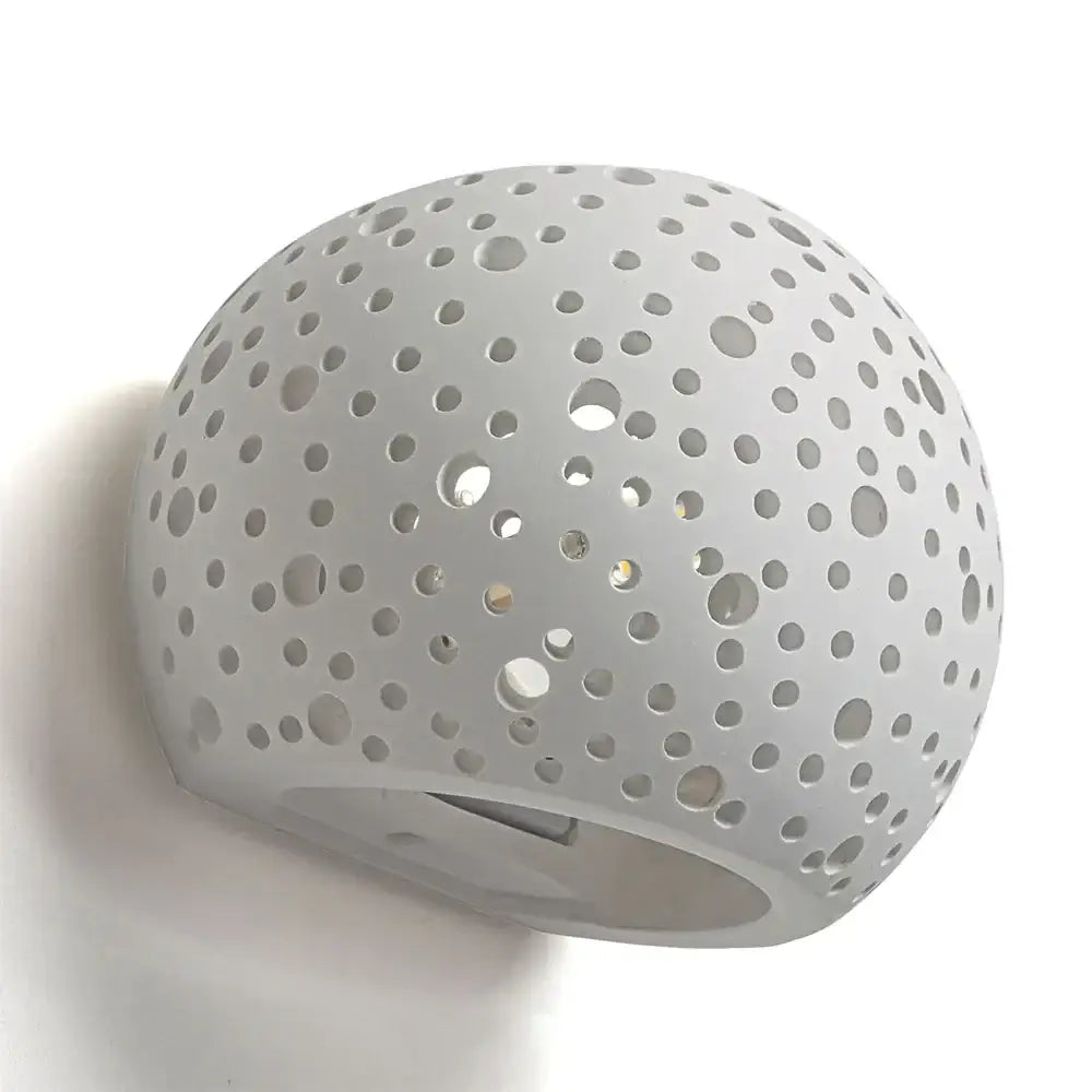 Minimalist white spherical gypsum wall lamp with circular perforations providing diffused light for living room