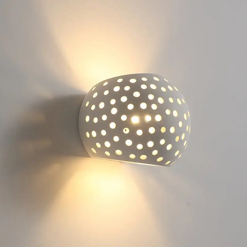 Minimalist off-white gypsum wall lamp with rounded perforations casting warm diffused light for living room