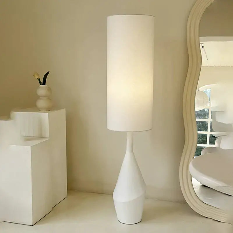 A minimalist white led floor lamp with a cylindrical shade and sculpted tapered geometric base for living room use