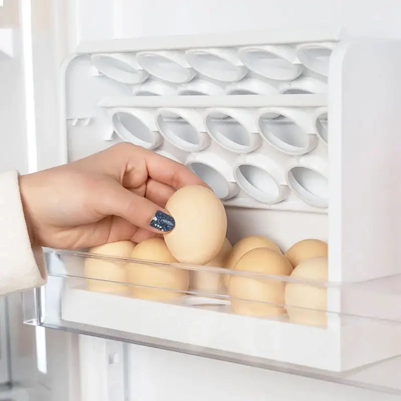 A hand holding a beige egg above a clear plastic egg storage rack in a minimalist white kitchen organizer