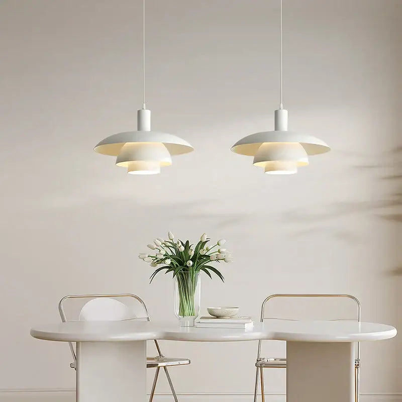 Two minimalist white pendant lights with layered design hang above dining table in decorbites cream style setting