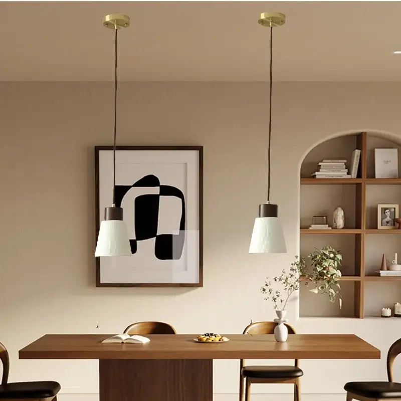 Two minimalist white pleated glass pendant lights with brass fixtures hang above a wooden dining table for home decor decorbites ceramic led