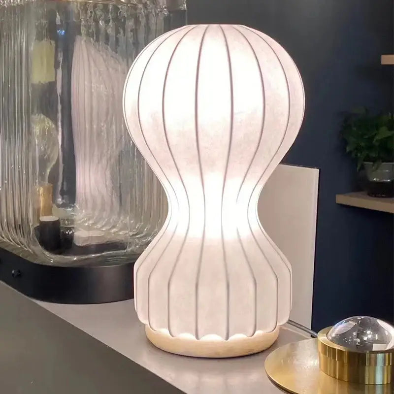 A modern minimalist white ribbed cocoon silk table lamp with a softly glowing rounded base for bedroom decorbites gatto cocoon