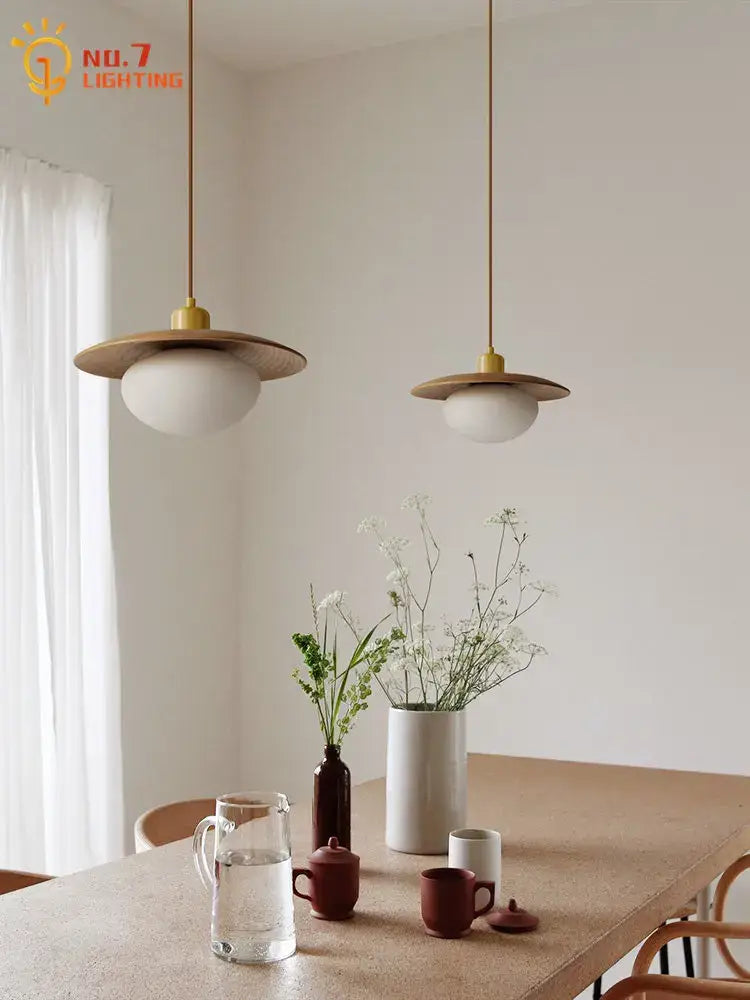 Two minimalist wood and brass pendant lights with cream wind frosted glass globes hanging above dining table