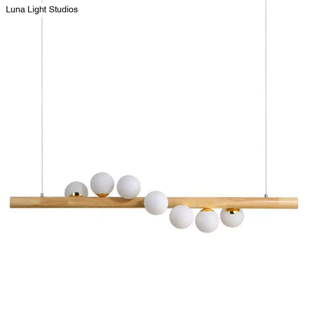 Modern minimalist linear island pendant with natural wood bar, six matte white glass globes, and gold metal accents for kitchen lighting