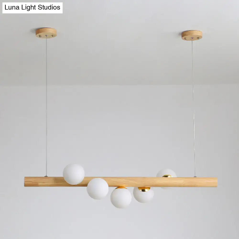 Minimalist wood and glass linear island pendant with natural wood bar white frosted glass spheres and brass accents for kitchen lighting
