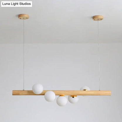 Minimalist wood and glass linear island pendant with natural wood bar white frosted glass spheres and brass accents for kitchen lighting