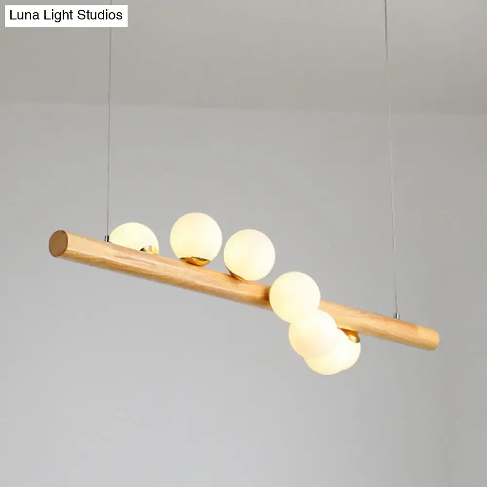 A minimalist linear island pendant with a natural wood beam and five frosted glass globe bulbs for kitchen lighting