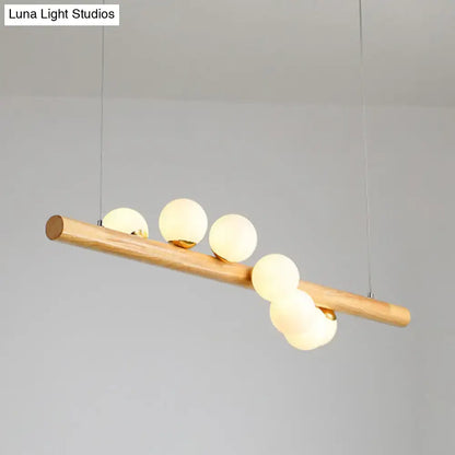 A minimalist linear island pendant with a natural wood beam and five frosted glass globe bulbs for kitchen lighting