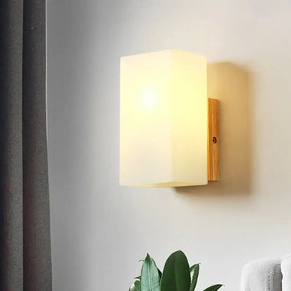 Minimalist warm-toned wall sconce with opal glass shade and natural wood backplate for bedroom wall light