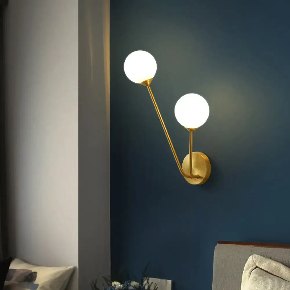 Minimalistic brass branch wall light features a gold-toned wall lamp with two frosted glass globes for bedroom use