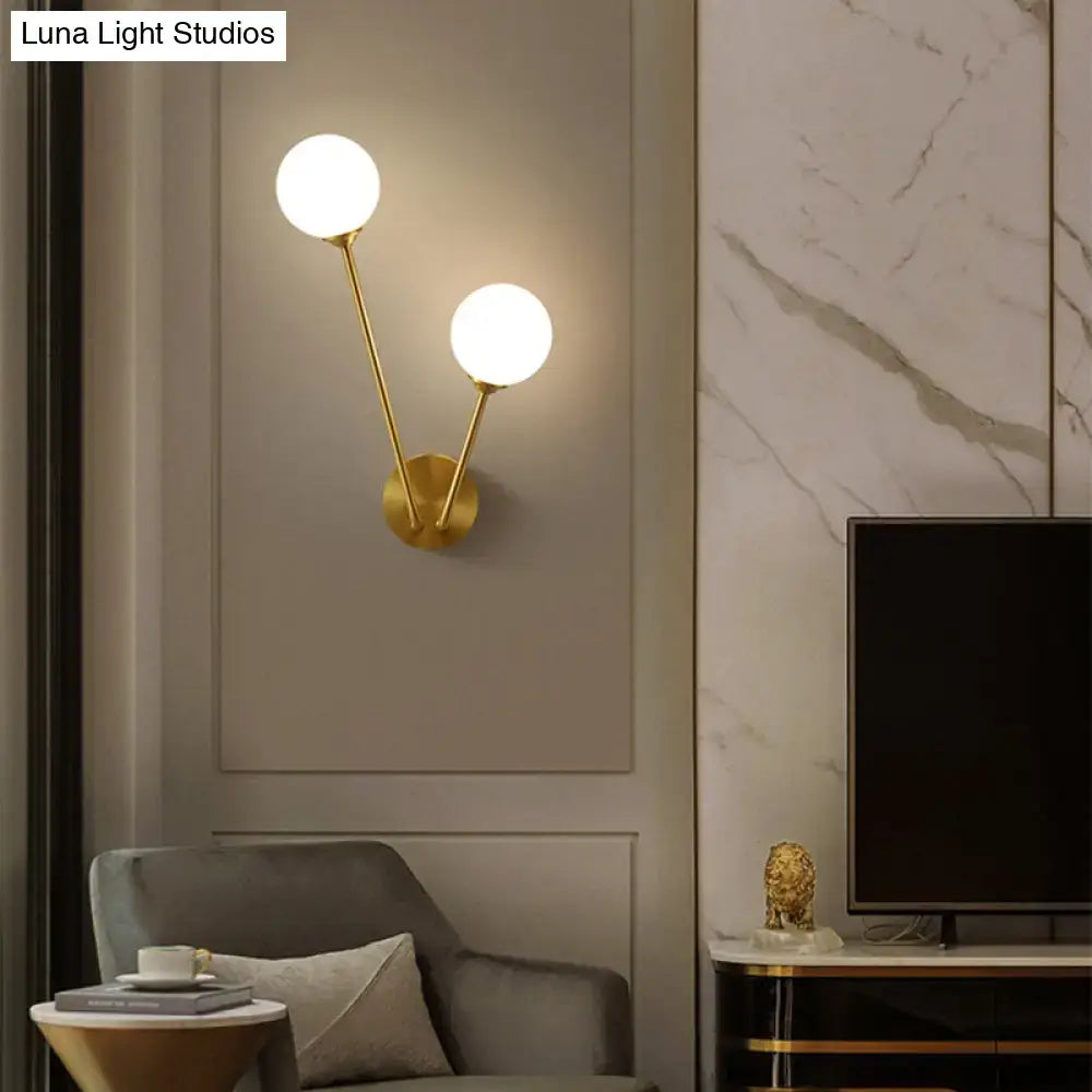 Minimalistic brass branch wall light with gold-toned finish and two frosted glass globes for bedroom wall lamp