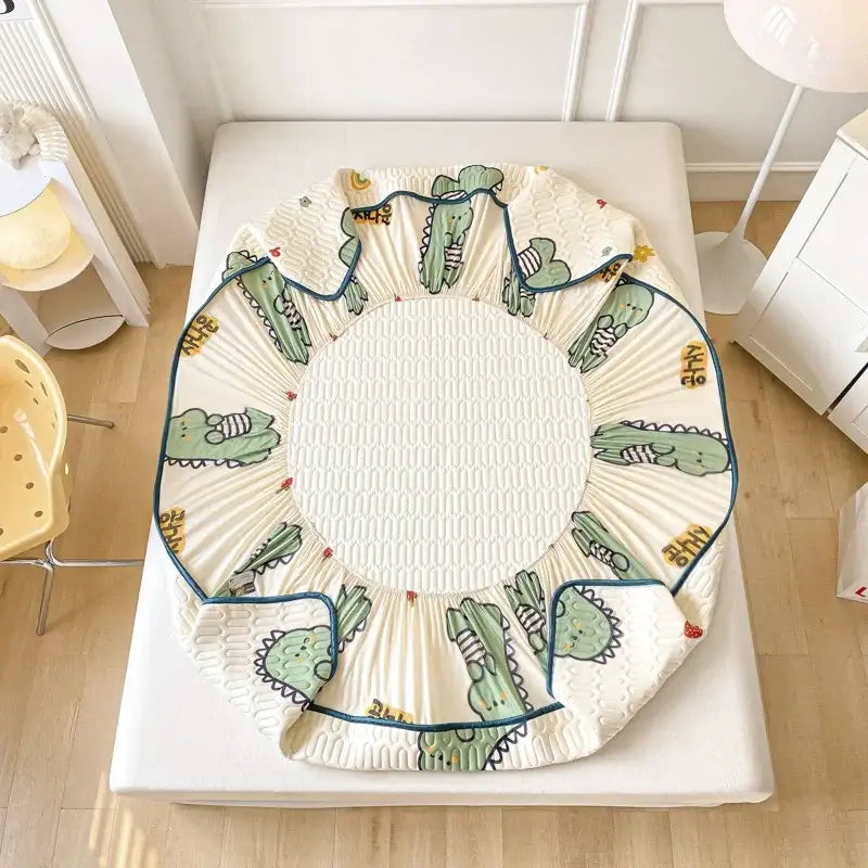 Cream-colored crocodile-patterned bed pad with ruffled edges and blue trim in mint green dinosaur latex fitted sheet set