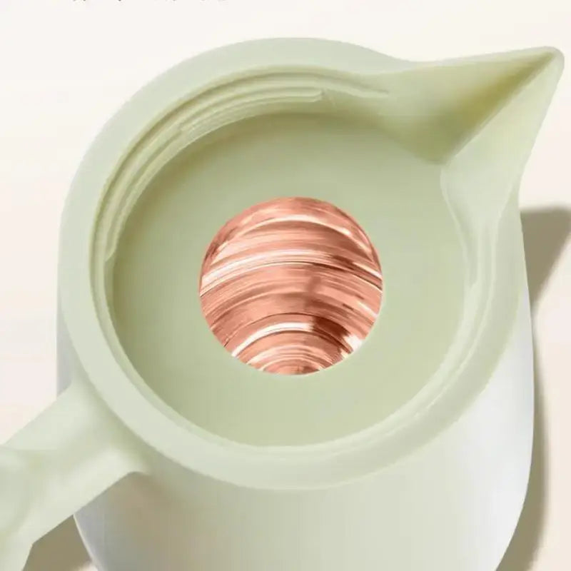 A matte sage green double glazed thermos kettle ceramic pitcher holds a reflective copper sphere inside